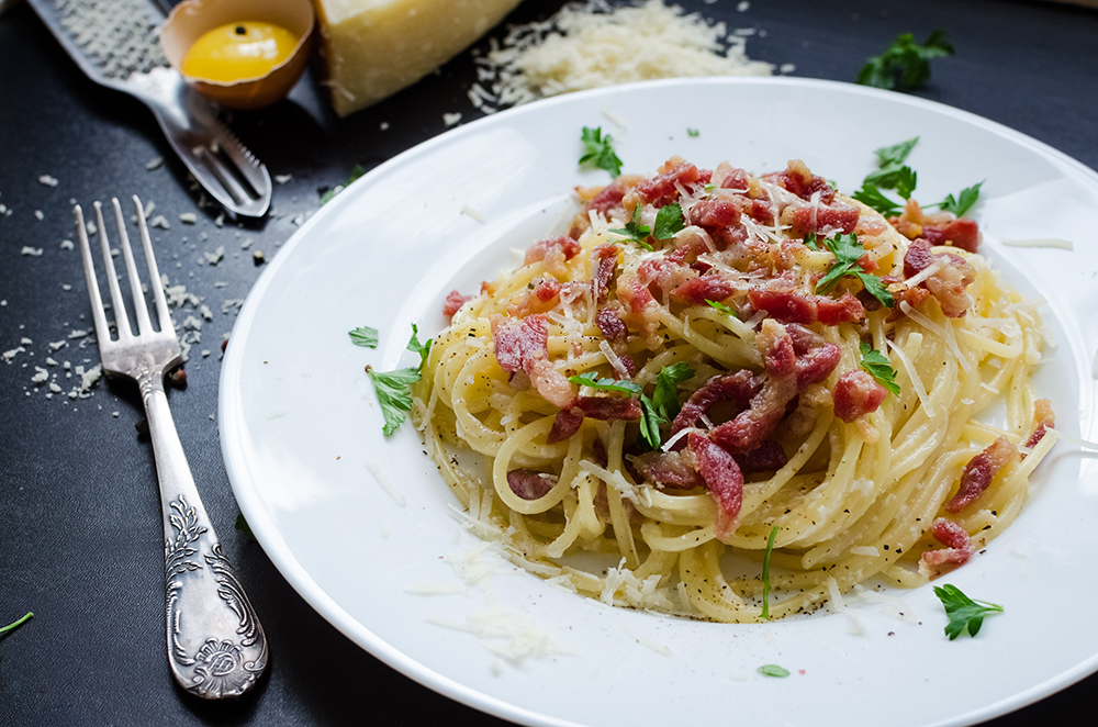 Pasta Carbonara. Spaghetti with bacon, parsel and parmesan cheese. Pasta Carbonara on white plate with parmesan on dark background. Italian food concept.